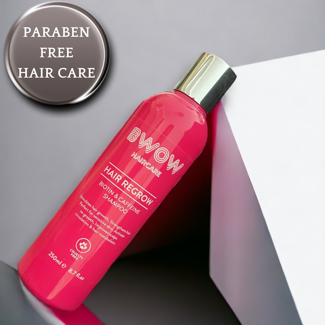 Pink bottle of BWOW Hair Regrow Biotin & Caffeine Shampoo with a silver cap, leaning against a white geometric shape, with the text "Paraben Free Hair Care" overlaid.