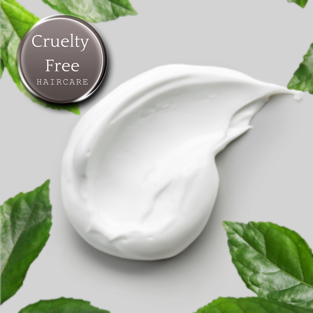 White cream smear on a gray background surrounded by green leaves, with the text "Cruelty Free Haircare" overlaid.